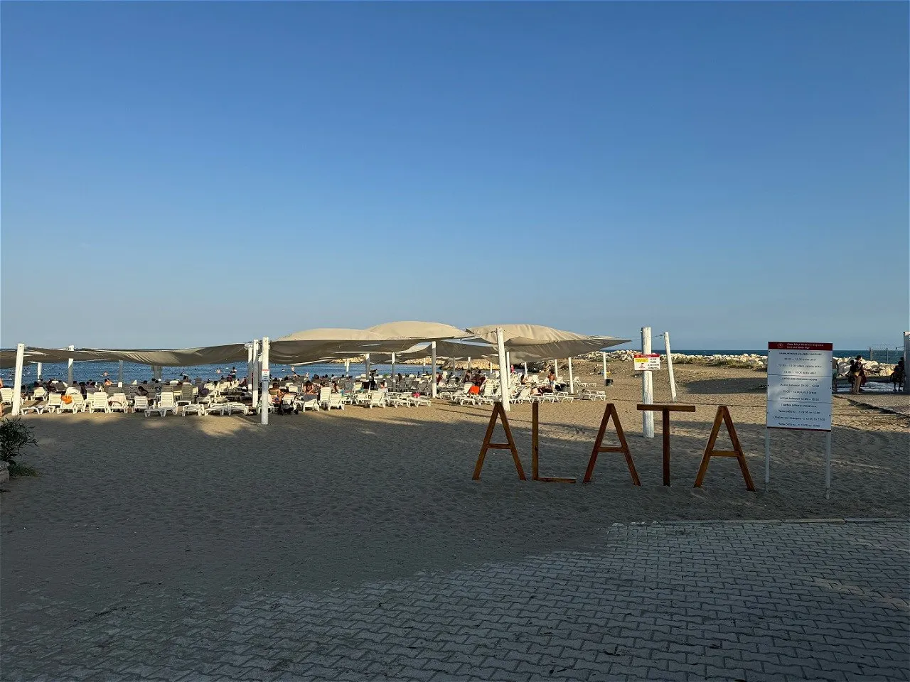 The Alata beach sign, with sunbeds and umbrellas behind it